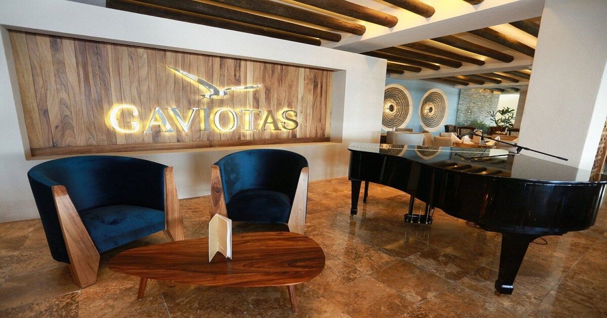 A reception area with a wooden wall, two blue chairs, a wooden coffee table, and a grand piano.