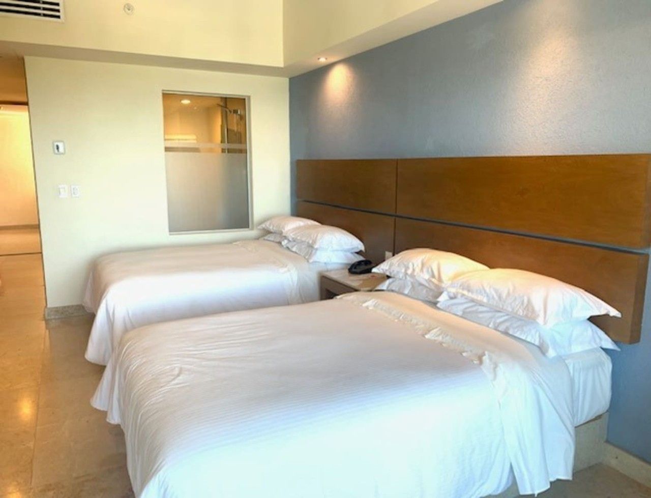 A hotel room with two single beds, a wooden headboard, a bedside table with a phone, and a bathroom door.