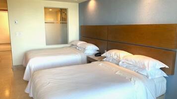 A hotel room with two single beds, a wooden headboard, a bedside table with a phone, and a bathroom door.