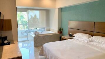 A hotel room with a bed, a small table, a chair, a window, and a bathroom with a bathtub.