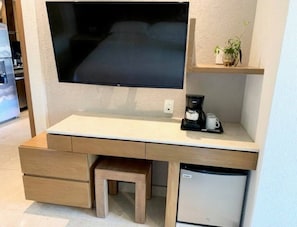 A compact workspace with a flat-screen TV, a coffee maker, and a small refrigerator.