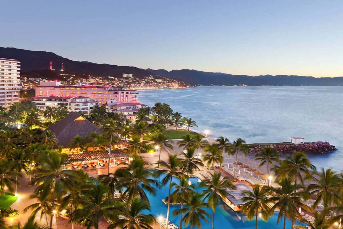 A resort with a large pool, palm trees, and a view of the ocean.