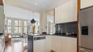A modern kitchen with white cabinetry, a stainless steel refrigerator, and a dishwasher. - Chic Chelsea maisonette with 2 terraces (London)