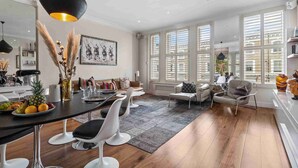 A spacious living area with a dining table, modern chairs, and a large window with blinds. - Chic Chelsea maisonette with 2 terraces (London)