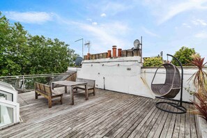 Una terraza de madera con una mesa y sillas, una silla colgante y antenas parabólicas en la azotea.