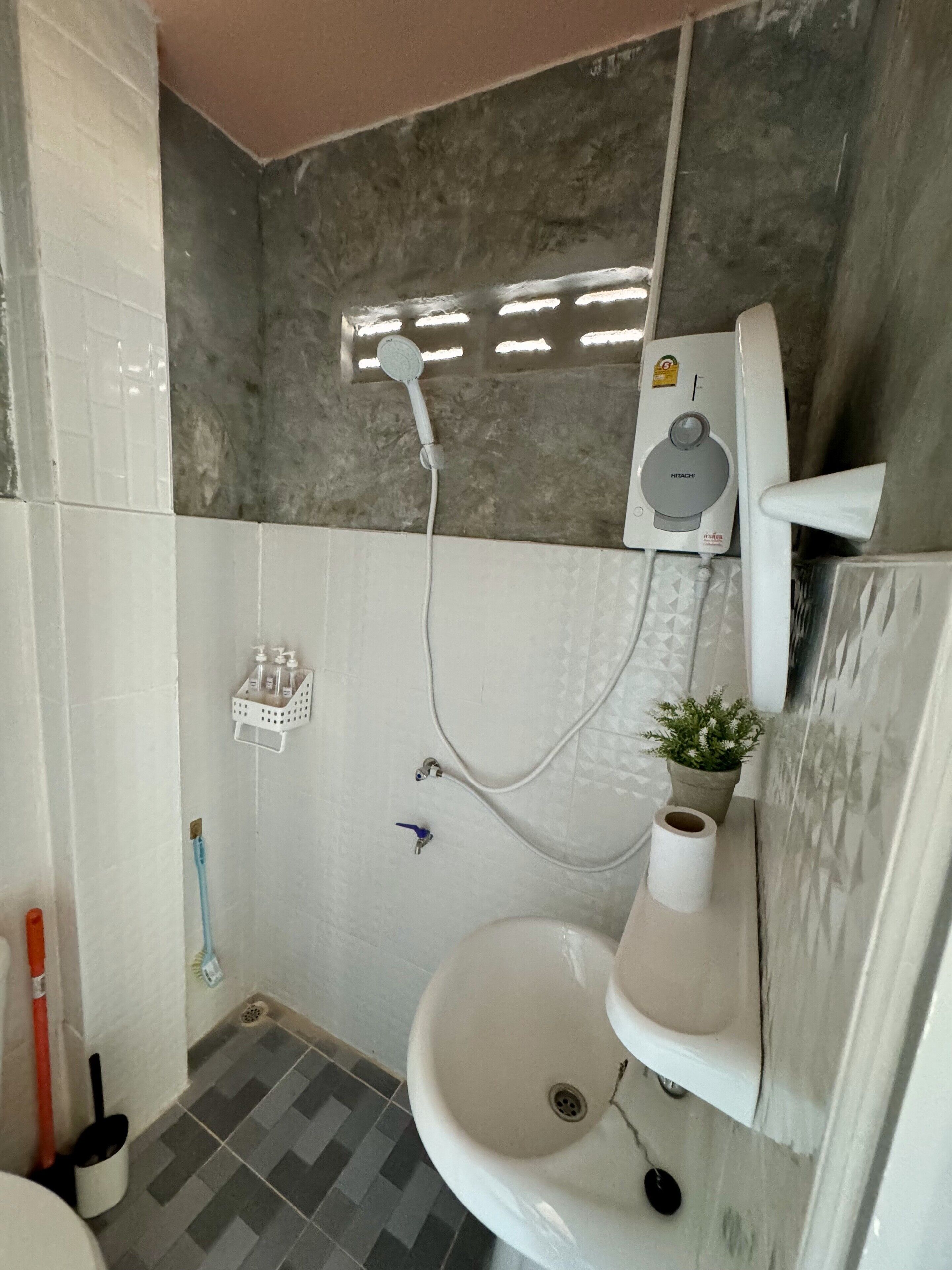 Ein Badezimmer mit einem weißen Waschbecken, einer Handbrause, einer Toilette und einem kleinen Topfpflanzen.