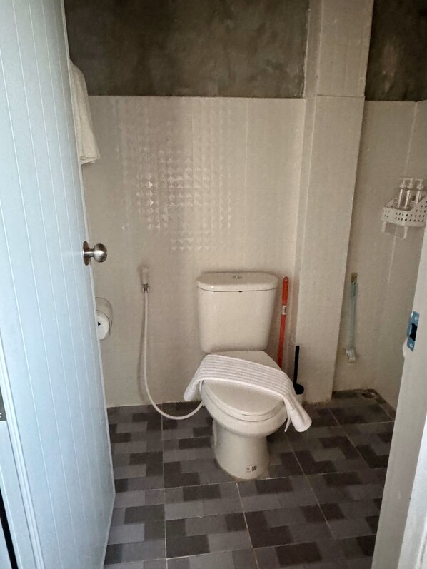 A small bathroom with a toilet, a towel hanging on the wall, and a shower area. - Sunshine Rest Resort (Ubon Ratchathani)