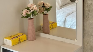 Ein Spiegel mit weißem Rahmen, zwei rosa Vasen mit Blumen und eine gelbe Schachtel auf einer weißen Kommode.