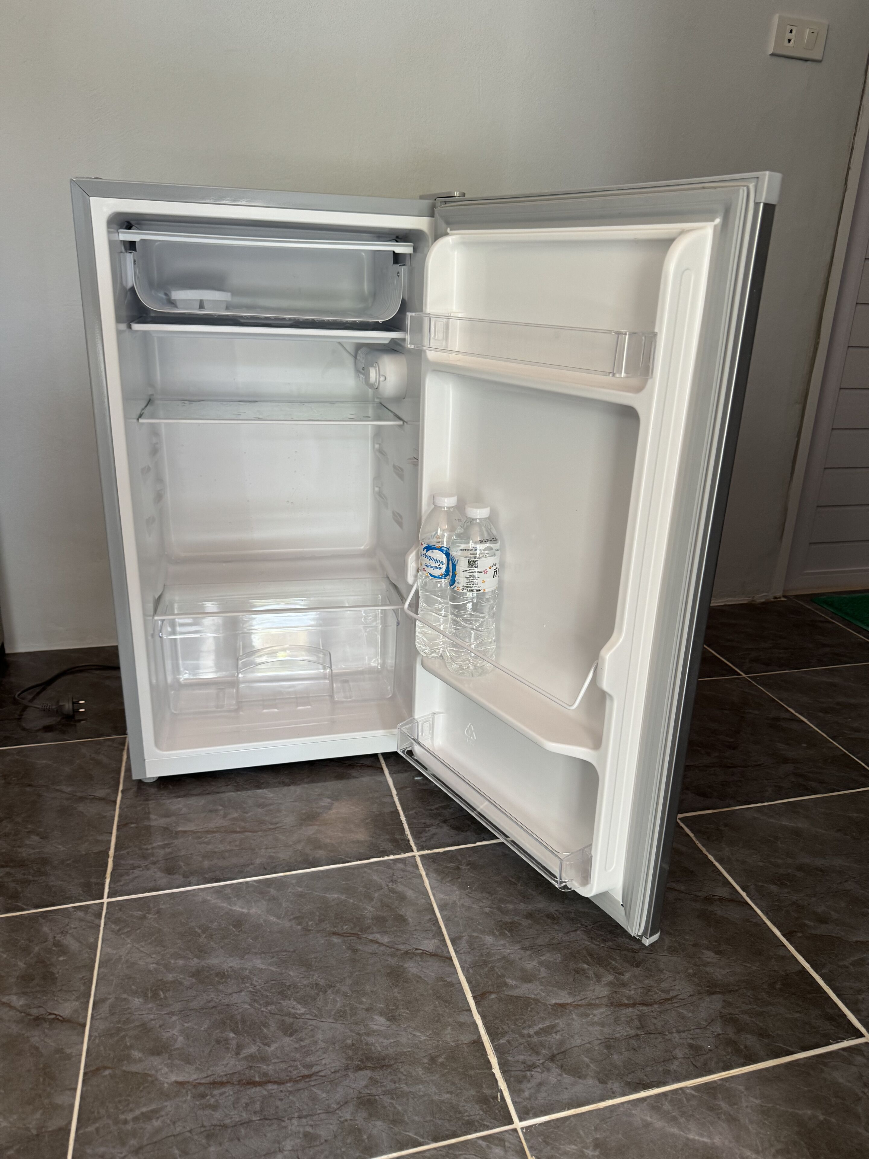 Un réfrigérateur ouvert, avec des étagères transparentes et une bouteille d’eau.