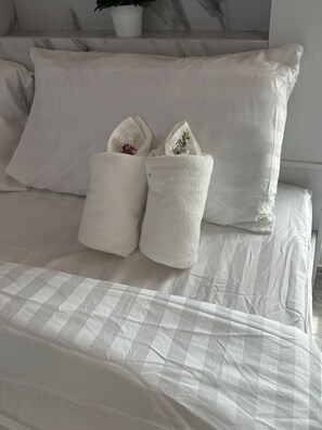A bed with white striped bedding, two white towels with flowers, and a potted plant on the headboard. - Sunshine Rest Resort (Ubon Ratchathani)