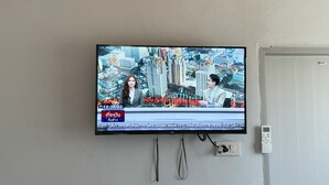 Ein an der Wand befestigter Fernseher zeigt eine Nachrichtensendung mit einer Stadtansicht im Hintergrund.