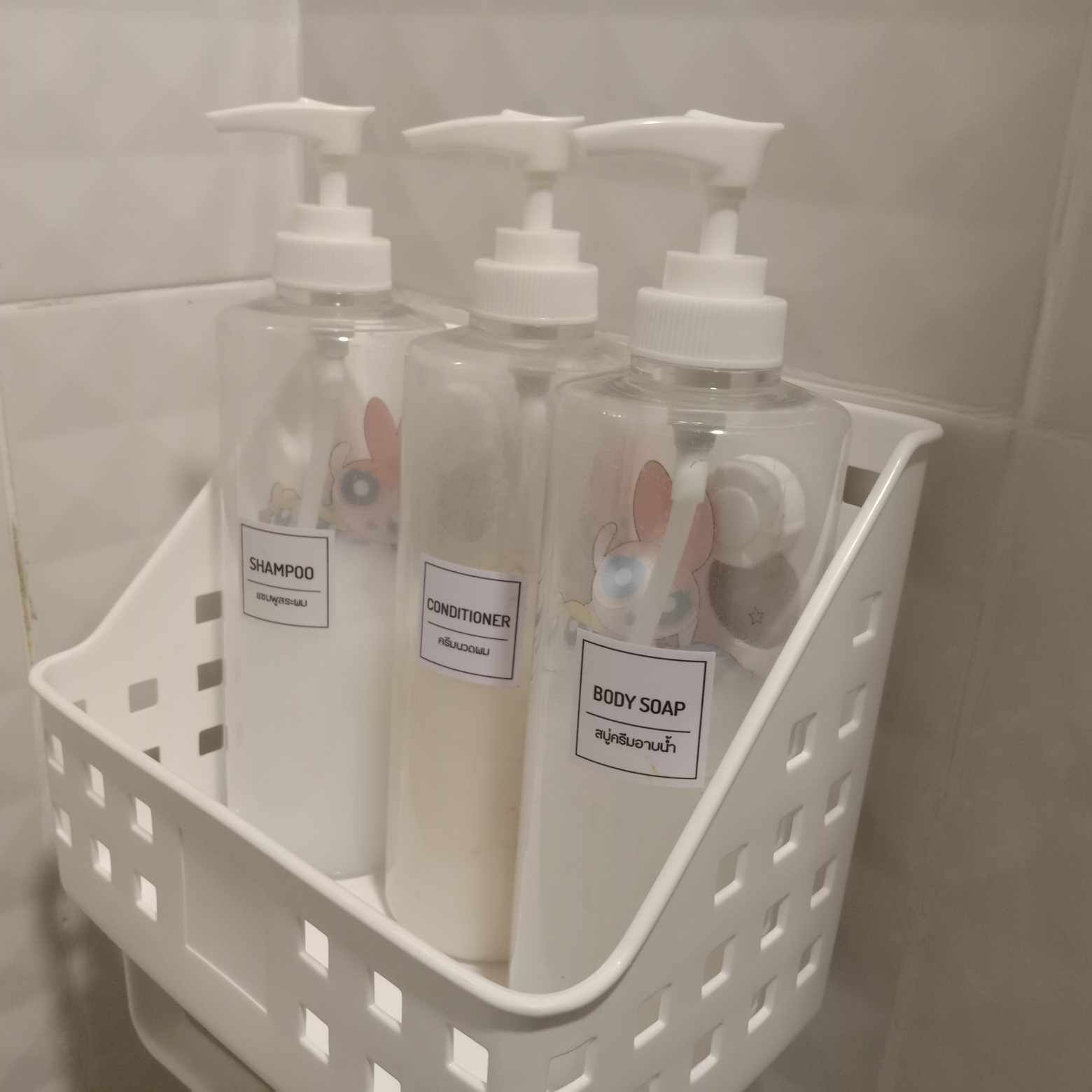 A white plastic basket containing three bottles of shampoo, conditioner, and body soap.
