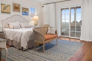Une chambre à coucher comprenant un lit, une chaise, une table de chevet, une lampe, un tapis à motifs et une grande fenêtre avec des rideaux.