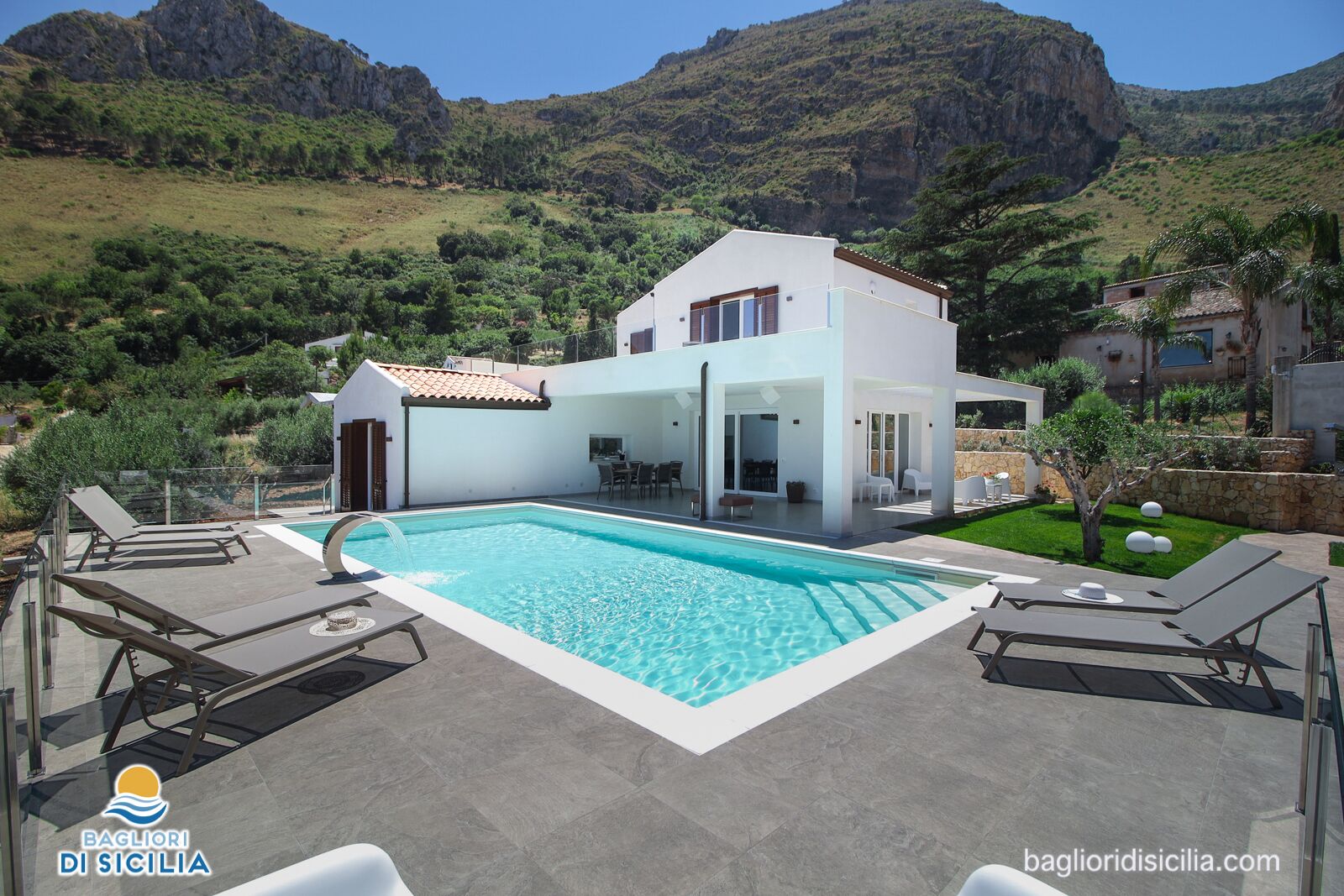 A modern house with a swimming pool, surrounded by lush greenery and mountains.