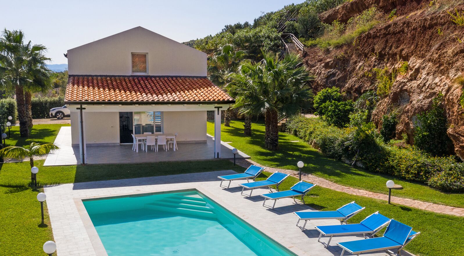 En modern villa med en swimmingpool, solstolar och en uteplats med utemöbler.