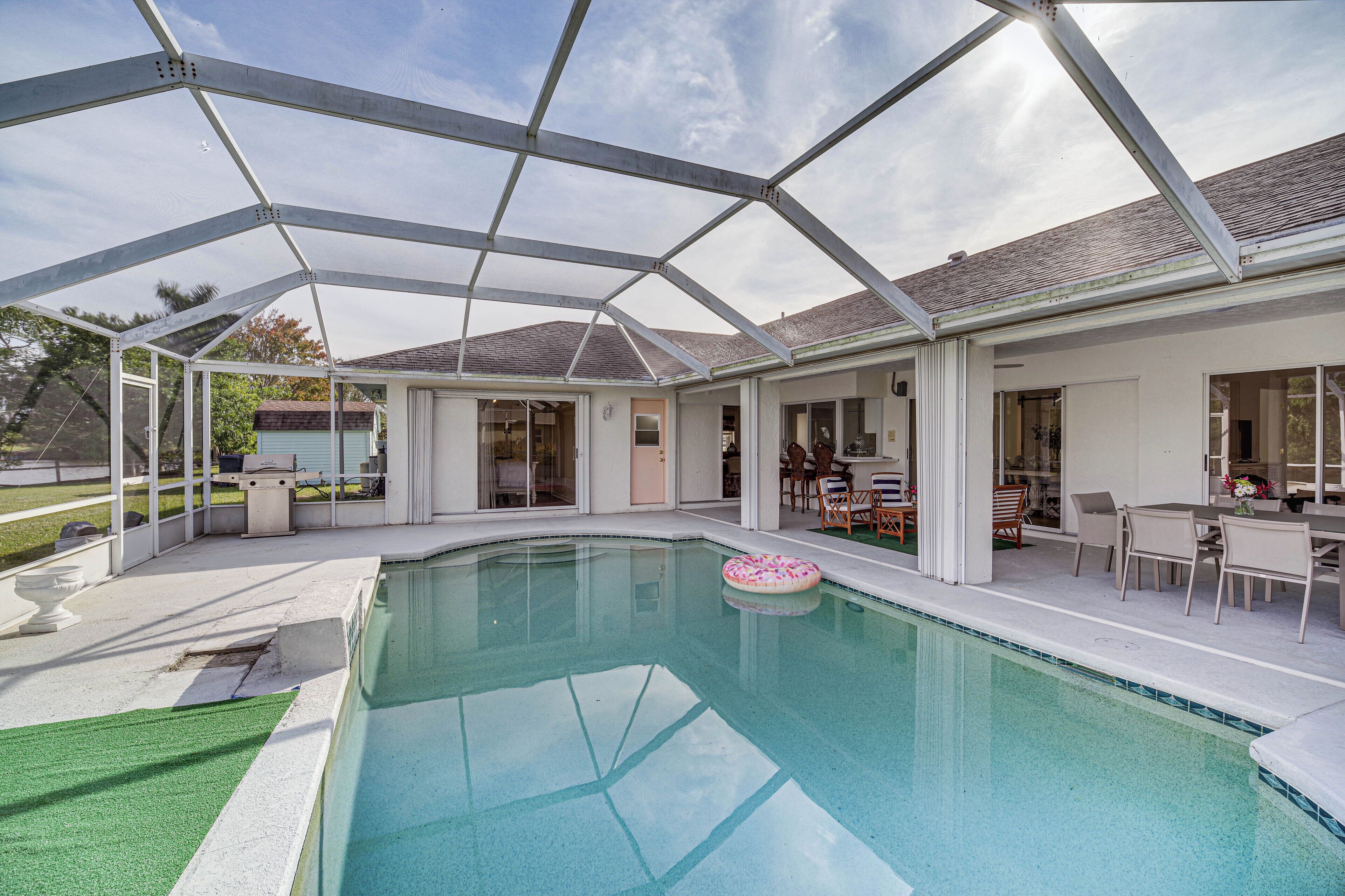 A covered swimming pool with a glass ceiling, a patio area with outdoor furniture, and a view of the house in the background.