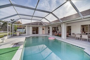 A covered swimming pool with a glass ceiling, a patio area with outdoor furniture, and a view of the house in the background. - Port St Lucie Canal-front Home w/ Heated Pool! (Port Saint Lucie)