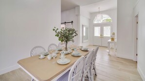 Comedor con una mesa dispuesta para seis personas, sillas blancas y un florero con plantas.