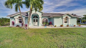 A two-story house with a light blue exterior, a front porch, and a palm tree. - Port St Lucie Canal-front Home w/ Heated Pool! (Port Saint Lucie)