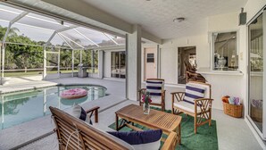 A covered outdoor pool area with wooden furniture, a ceiling fan, and a view of the surrounding landscape. - Port St Lucie Canal-front Home w/ Heated Pool! (Port Saint Lucie)