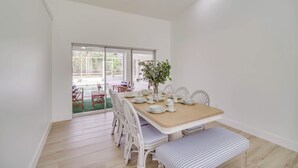 A dining area with a wooden table, white chairs, and a bench. There is a potted plant on the table. - Port St Lucie Canal-front Home w/ Heated Pool! (Port Saint Lucie)