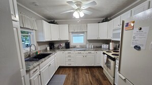 A kitchen with white cabinets, a granite countertop, a ceiling fan, a refrigerator, and a wooden floor.