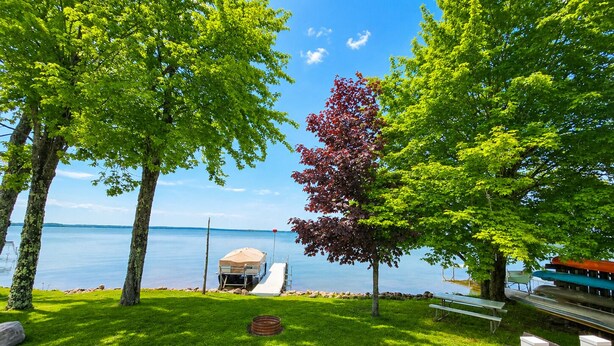A lakeside deck with a covered seating area, a small boat dock, and a grassy lawn.