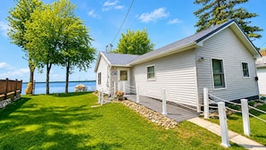 A white single-story house with a small porch, a deck, and a view of a lake.