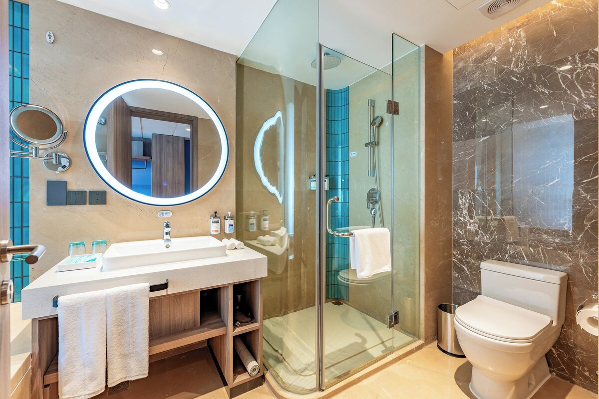 A modern bathroom with a glass-enclosed shower, a white sink with a mirror, and a marble wall.
