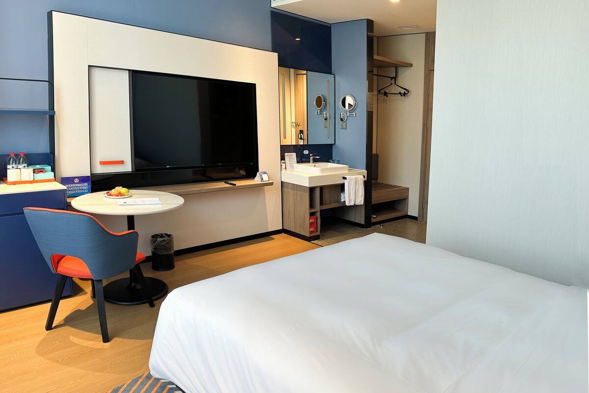 A hotel room with a bed, a TV, a desk with a chair, a sink, and a mirror.