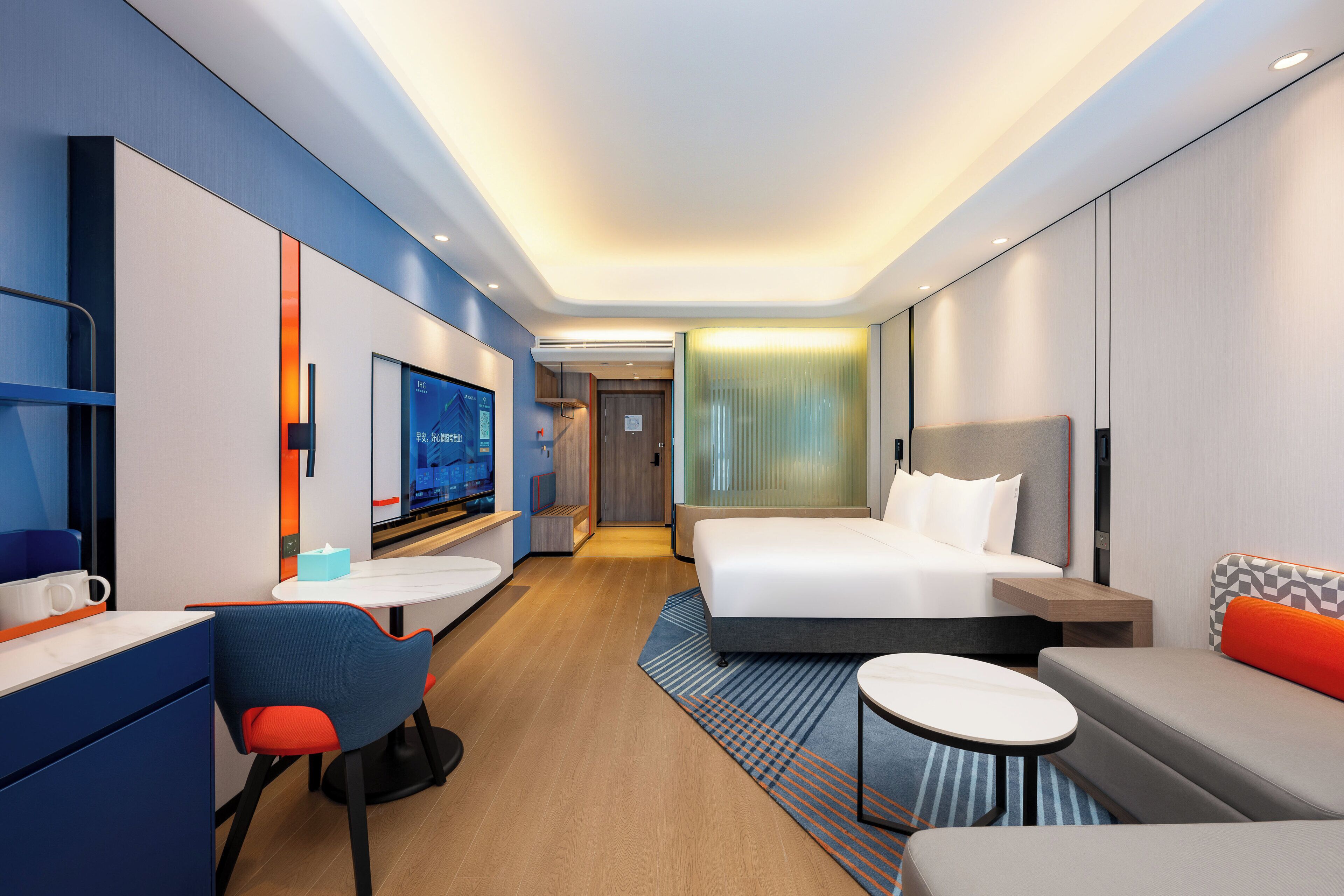 A modern hotel room with a bed, a desk, a chair, a sofa, and a TV.