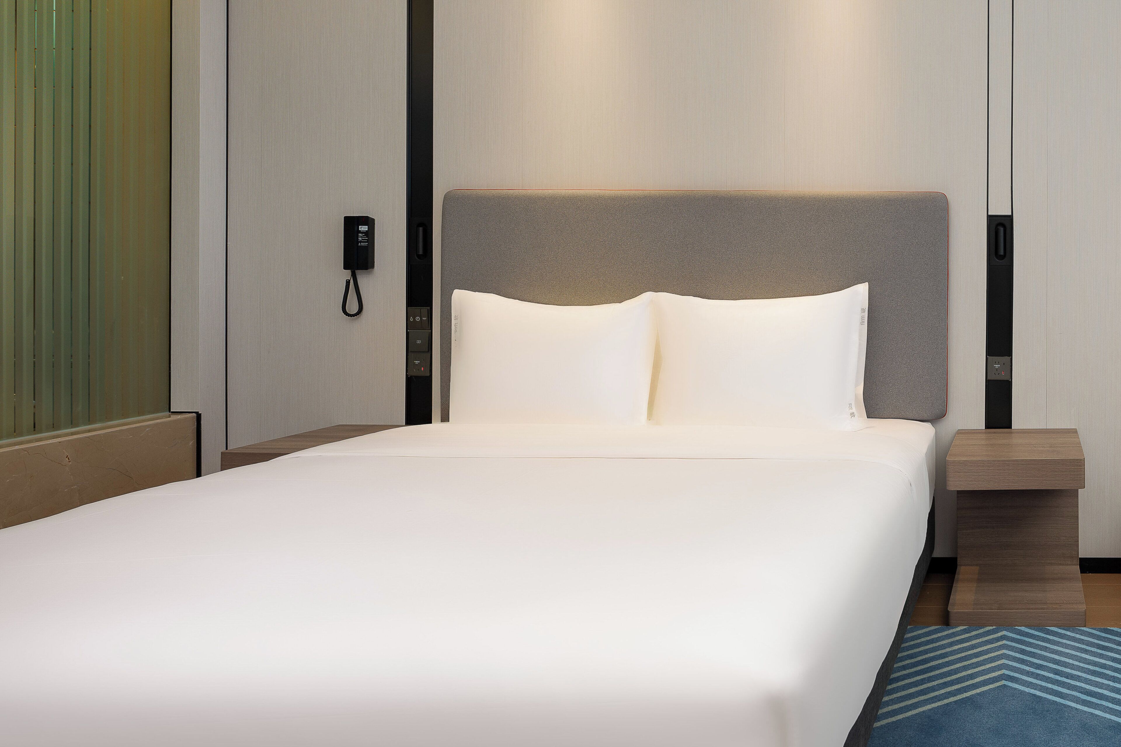 A hotel room with a large bed, a bedside table, a nightstand, and a wall-mounted phone.