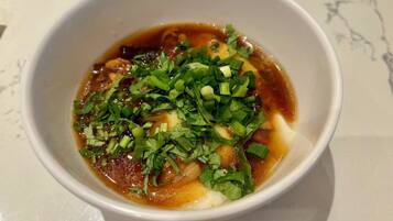 A bowl of soup with green onions and cilantro on a white surface.
