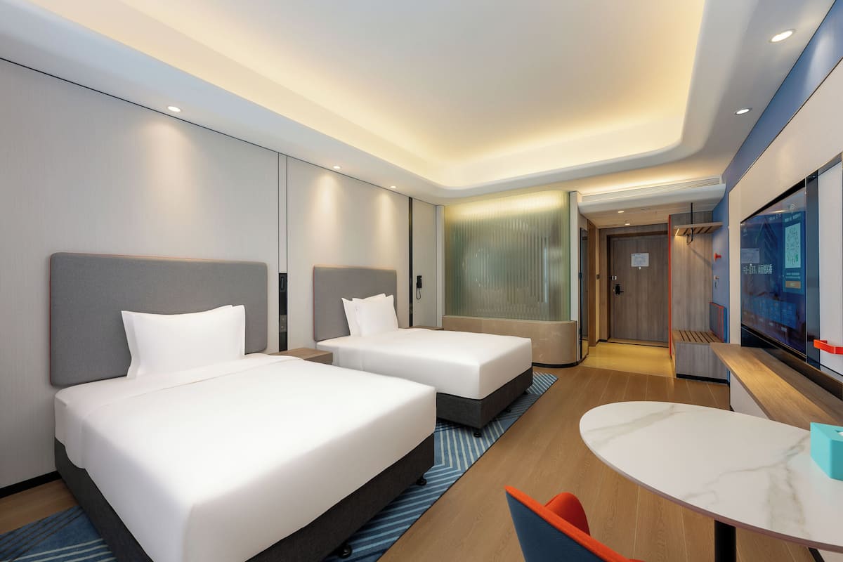 A hotel room with two beds, a small table, and a TV.