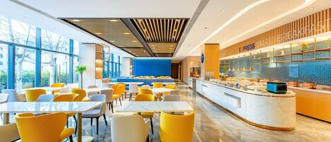 A modern hotel lobby with a breakfast bar, seating area, and large windows.