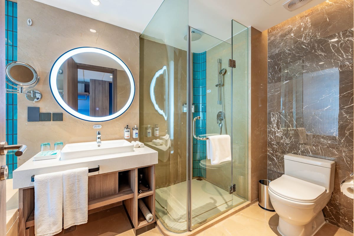 A modern bathroom with a glass-enclosed shower, a white sink with a mirror, and a marble wall.