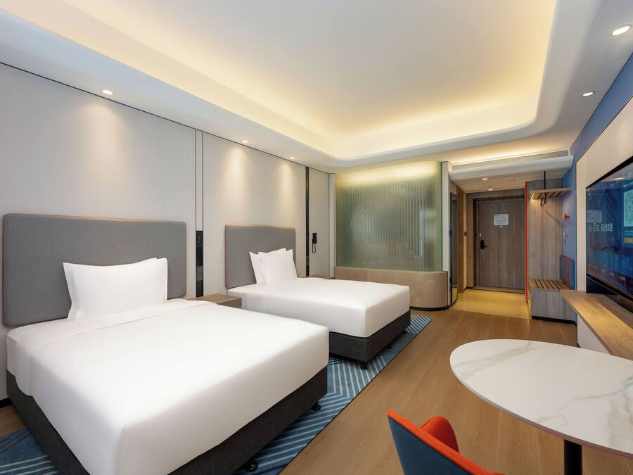 Quarto de hotel com duas camas, uma mesinha e uma televisão.