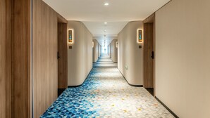 A hotel hallway with a geometric patterned floor, wooden paneling on the walls, and illuminated signs indicating room numbers. - Holiday Inn Express Beijing Conference Center by IHG (Beijing)