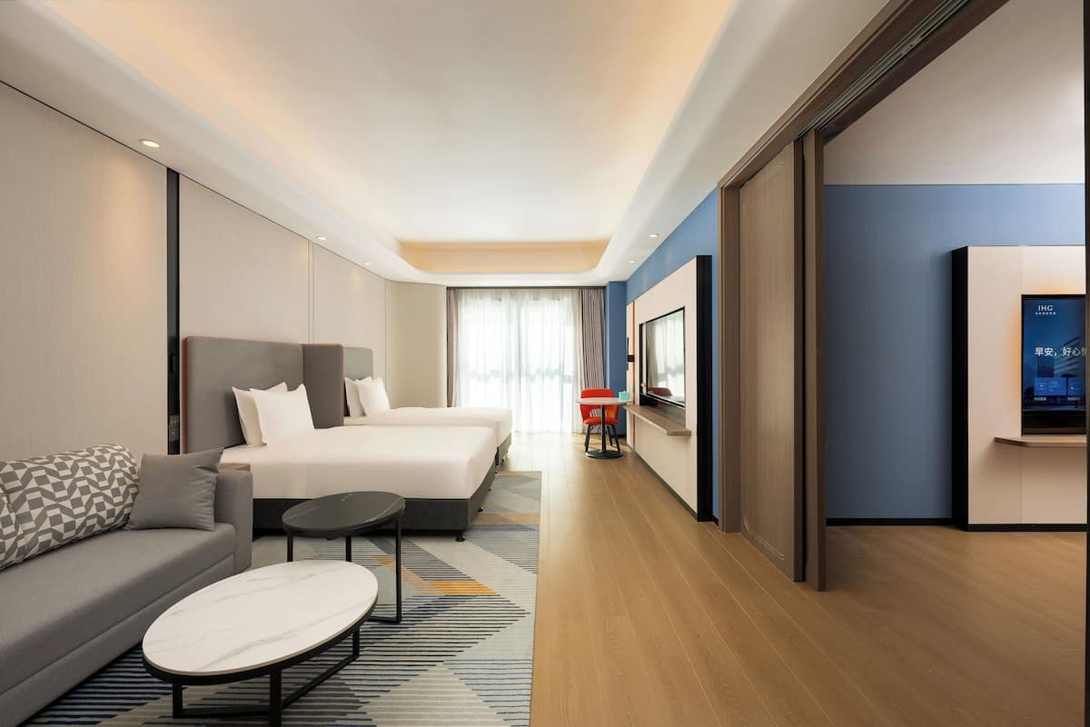 A modern hotel room with a large bed, a sofa, a small table, and a TV.