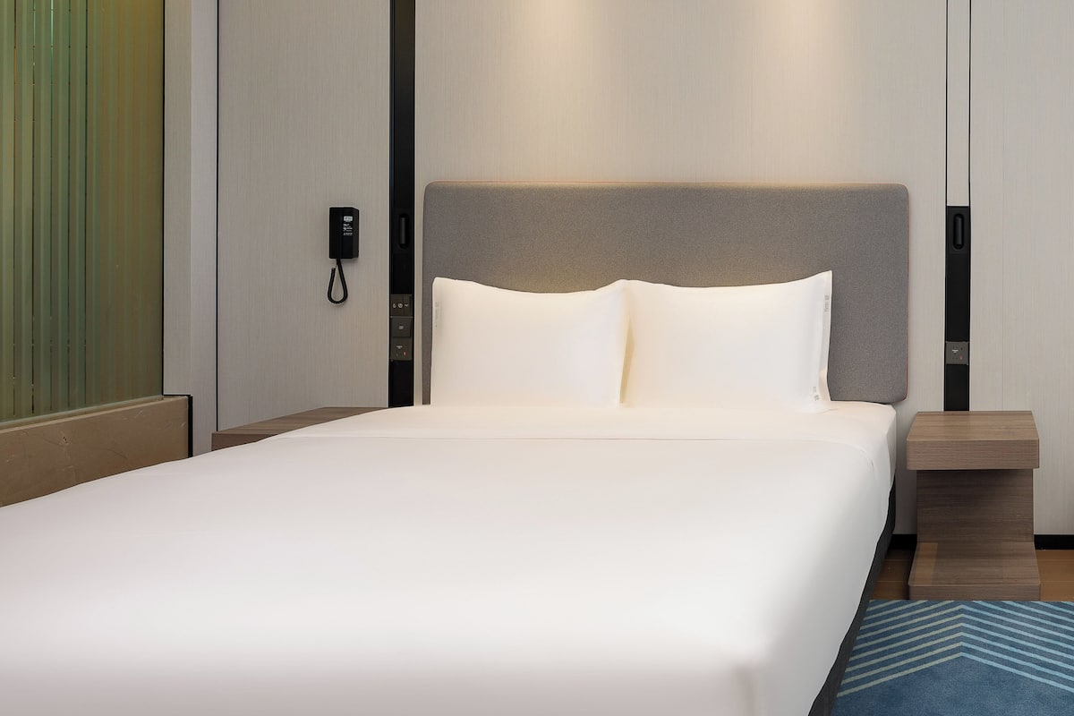 A hotel room with a large bed, a bedside table, a nightstand, and a wall-mounted phone.