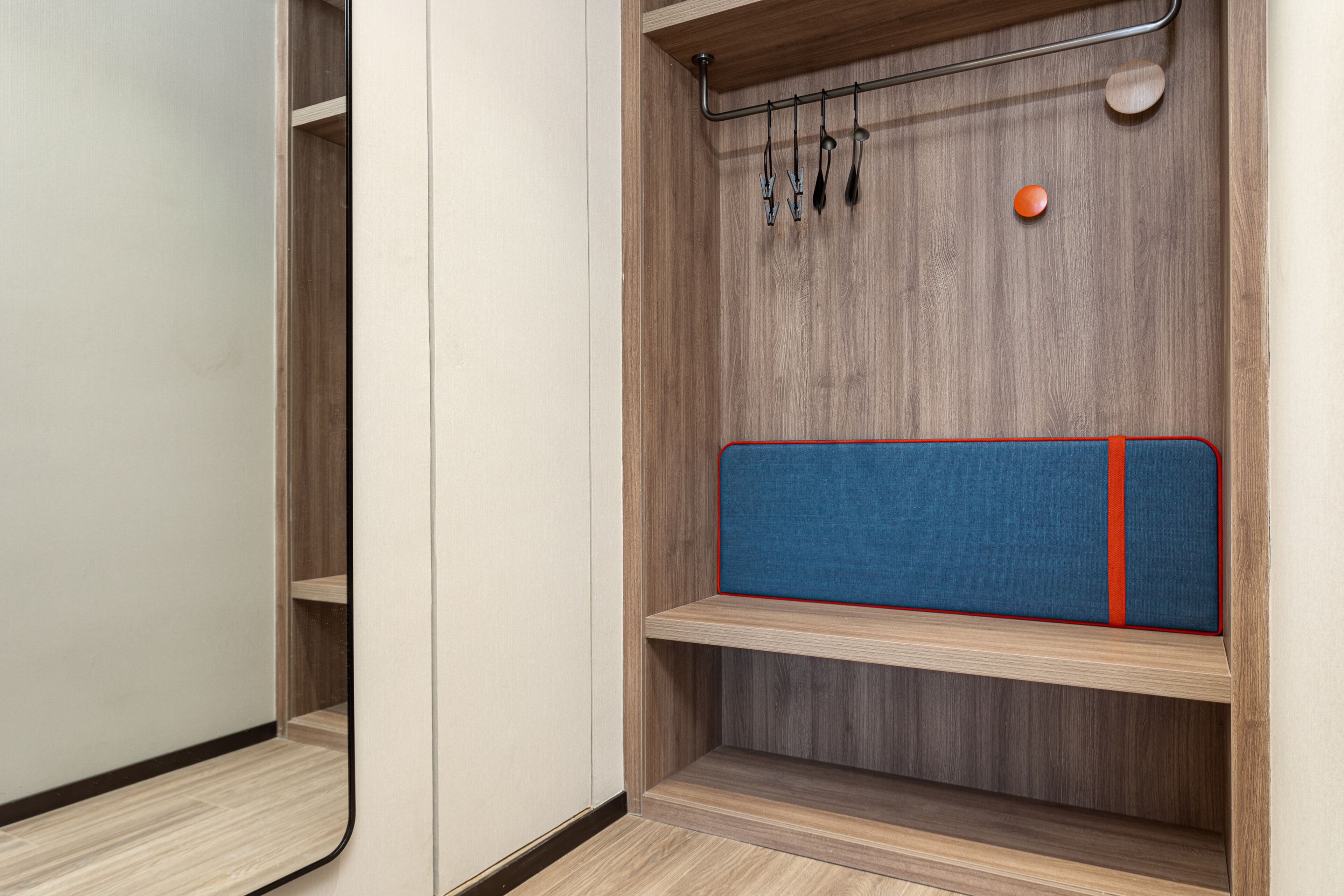 A wooden wardrobe with a mirror, a hanging rack, and a blue padded shelf.