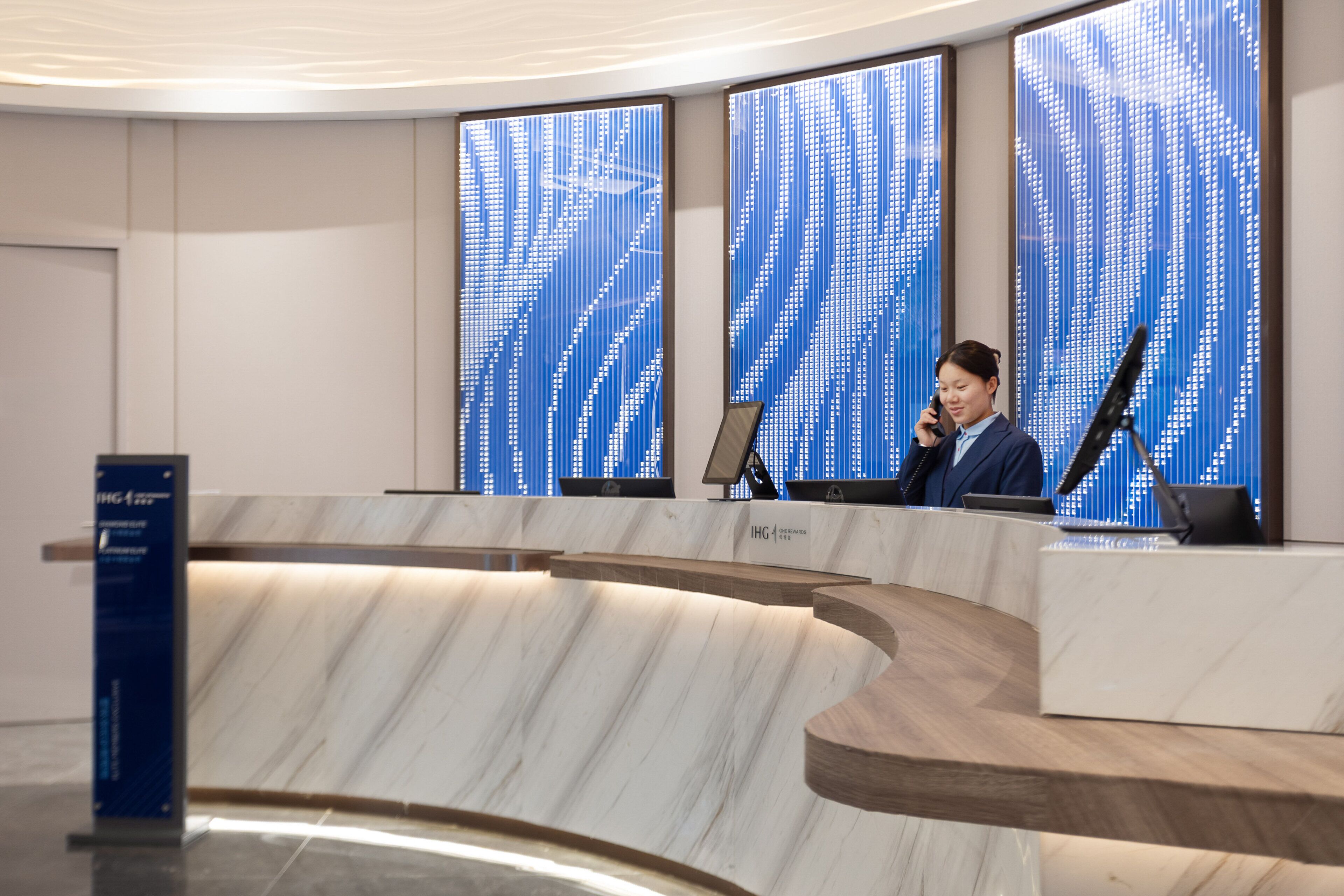 A reception desk with a modern design, featuring a marble countertop and a digital display wall in the background.