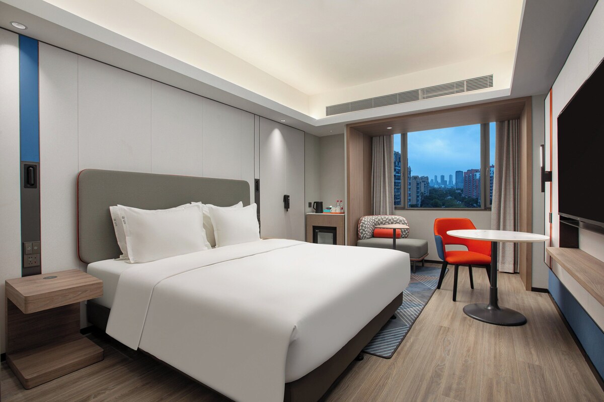 Habitació d'hotel moderna amb un llit gran, un escriptori, una cadira i vista a la ciutat.