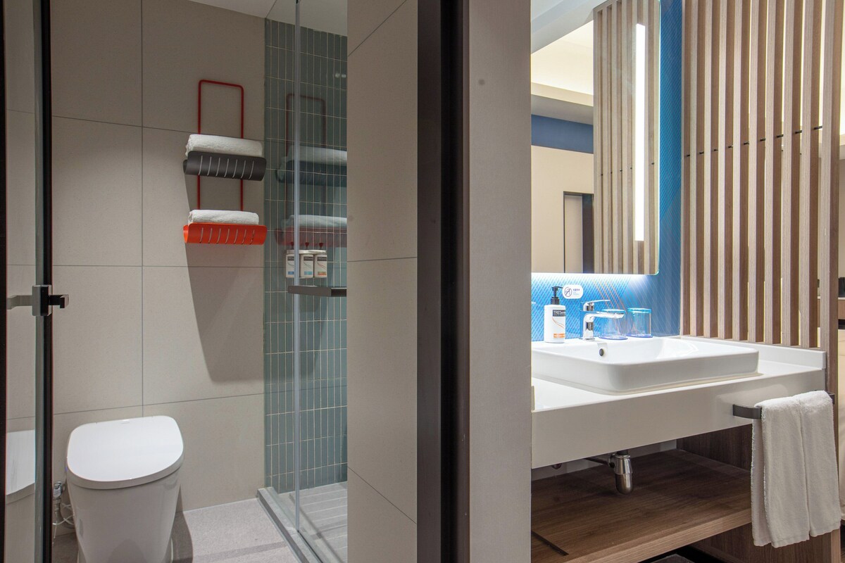 Un bany modern amb una cabina de dutxa de vidre, un vàter blanc i un lavabo blanc amb un mirall a la part superior.