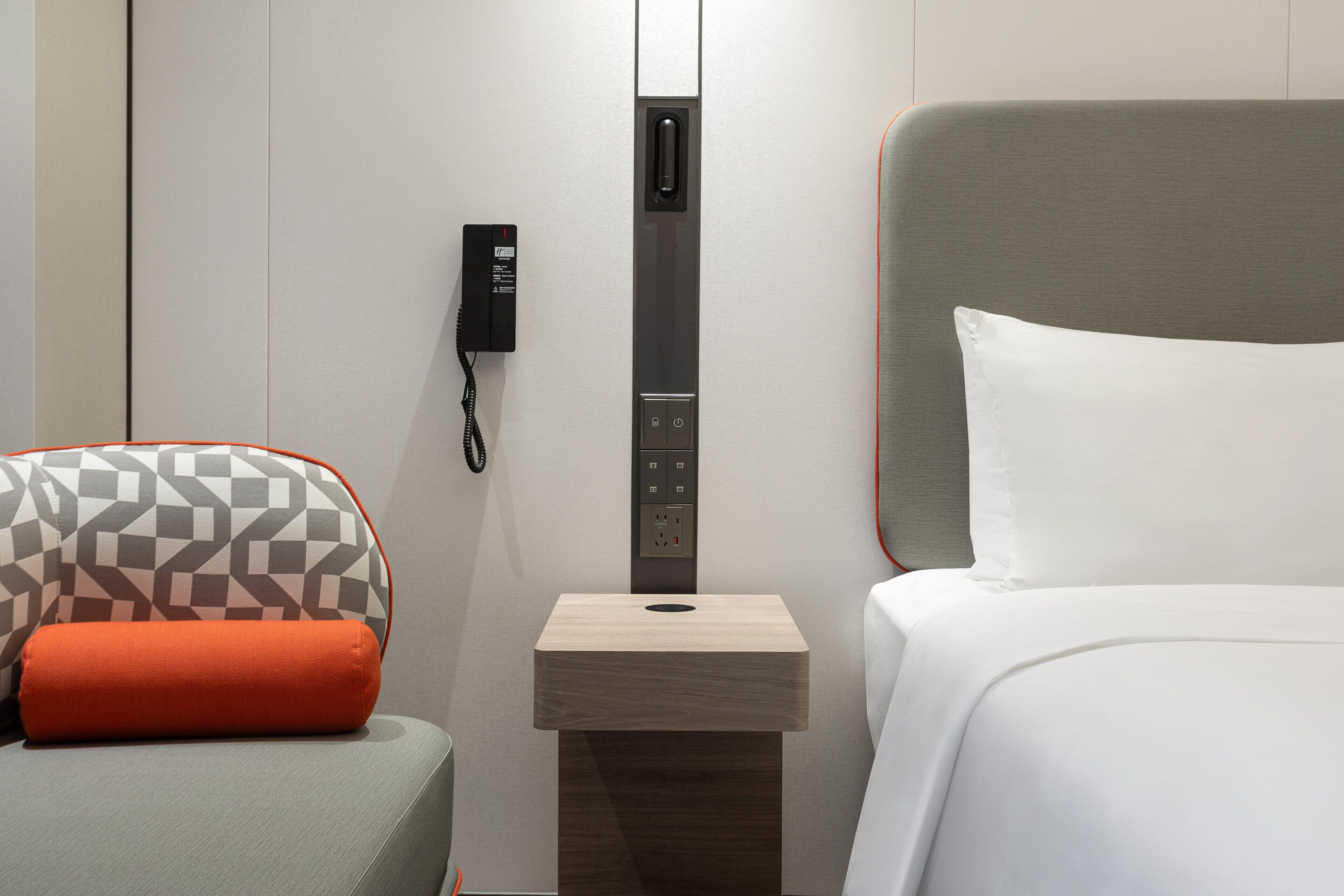 Een hotelkamer met een bed, een nachtkastje met een telefoon en een gestreept kussen.