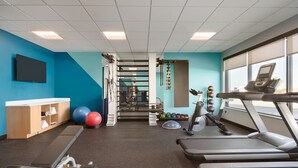 Une salle de sport équipée de tapis de course, de ballons d’exercice et d’un téléviseur fixé au mur.