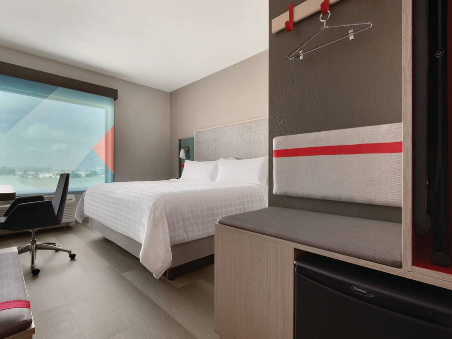 A hotel room with a bed, a desk, a chair, and a small kitchenette.