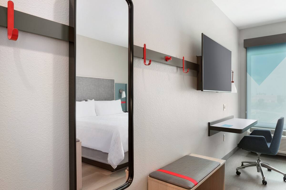 Habitación de hotel con cama, escritorio, silla, televisor montado en la pared y ventana con vistas.