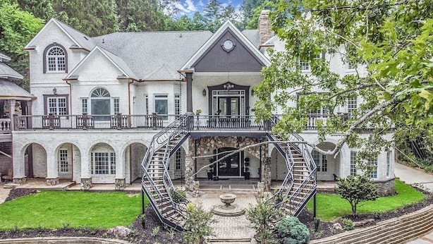 A large, two-story house with a central staircase, a covered porch, and a well-maintained lawn.
