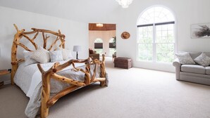 A spacious bedroom with a unique wooden bed frame, a large window with a view, and a cozy seating area.